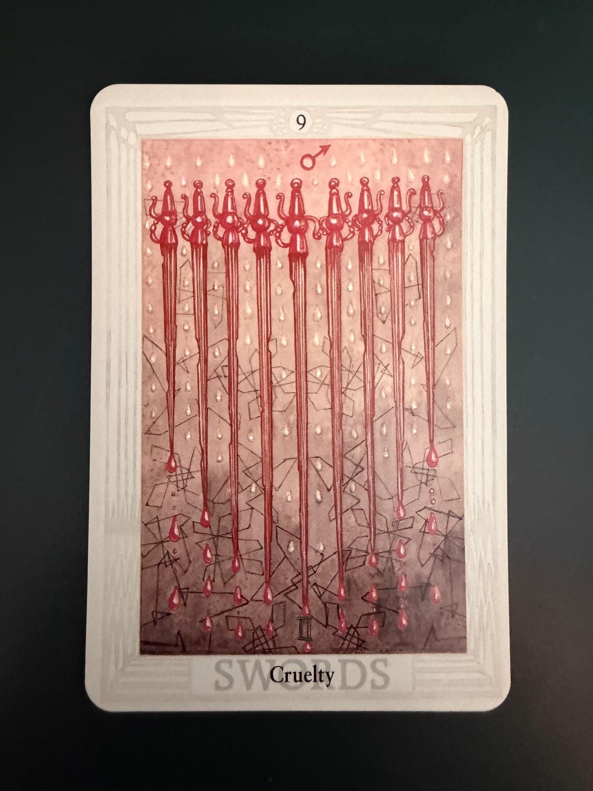 Nine of Swords, titled “Cruelty,” from Claire Gilman’s Thoth Tarot deck, with nine long red swords descending through a pink and grey field of droplets and fractured lines.