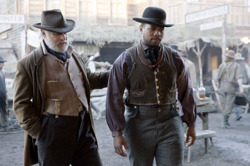 This image shows George Hearst (played by Gerald McRaney) on the left and Odell Marchbanks (played by Omar Gooding) on the right. Both men walk down Deadwood's main thoroughfare. This image shows George Hearst (played by Gerald McRaney) on the left and Odell Marchbanks (played by Omar Gooding) on the right. Both men walk down Deadwood's main thoroughfare.