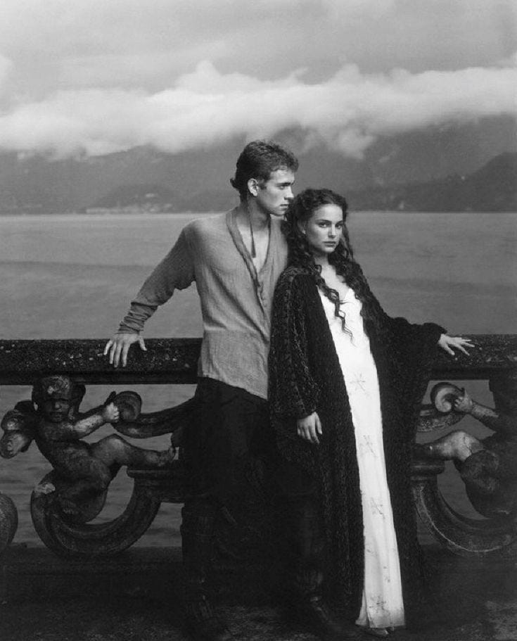 This may contain: a man and woman standing next to each other on a bridge near the water with mountains in the background This may contain: a man and woman standing next to each other on a bridge near the water with mountains in the background
