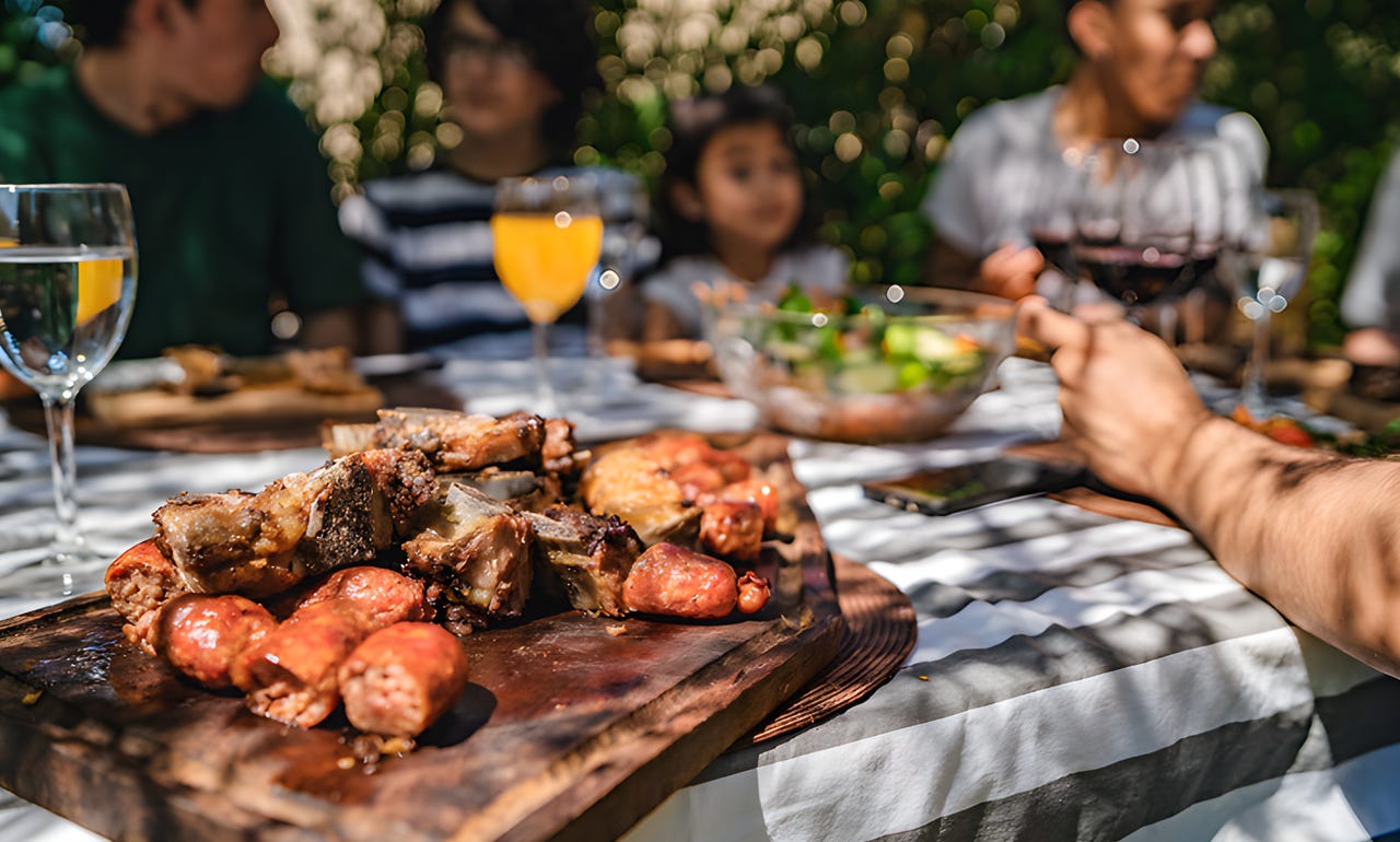 Platter of meats on a picnic table with family in background.