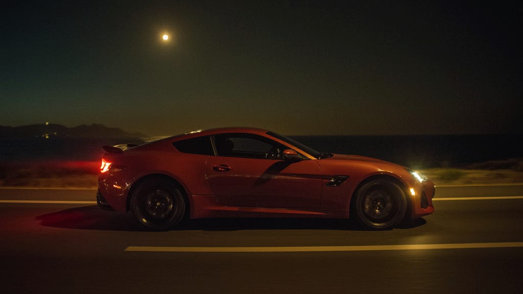 a red sport car with 2 doors, racing on a highway by the coast, moody, cinematic, at night