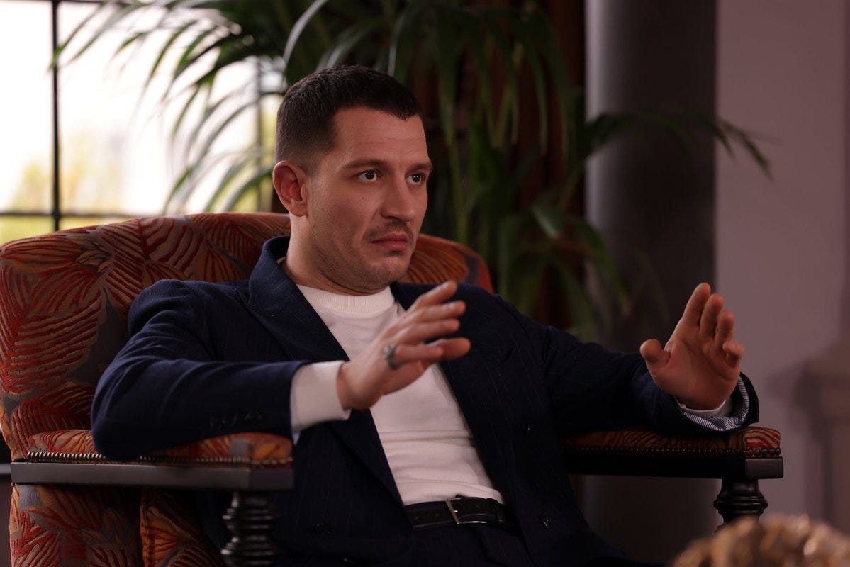 Uraz Kaygılaroğlu röportajda konuşurken — lacivert ceket, renkli koltuk Uraz Kaygılaroğlu röportajda konuşurken — lacivert ceket, renkli koltuk