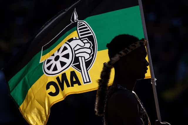 Person silhouetted against black, green and yellow flag Person silhouetted against black, green and yellow flag