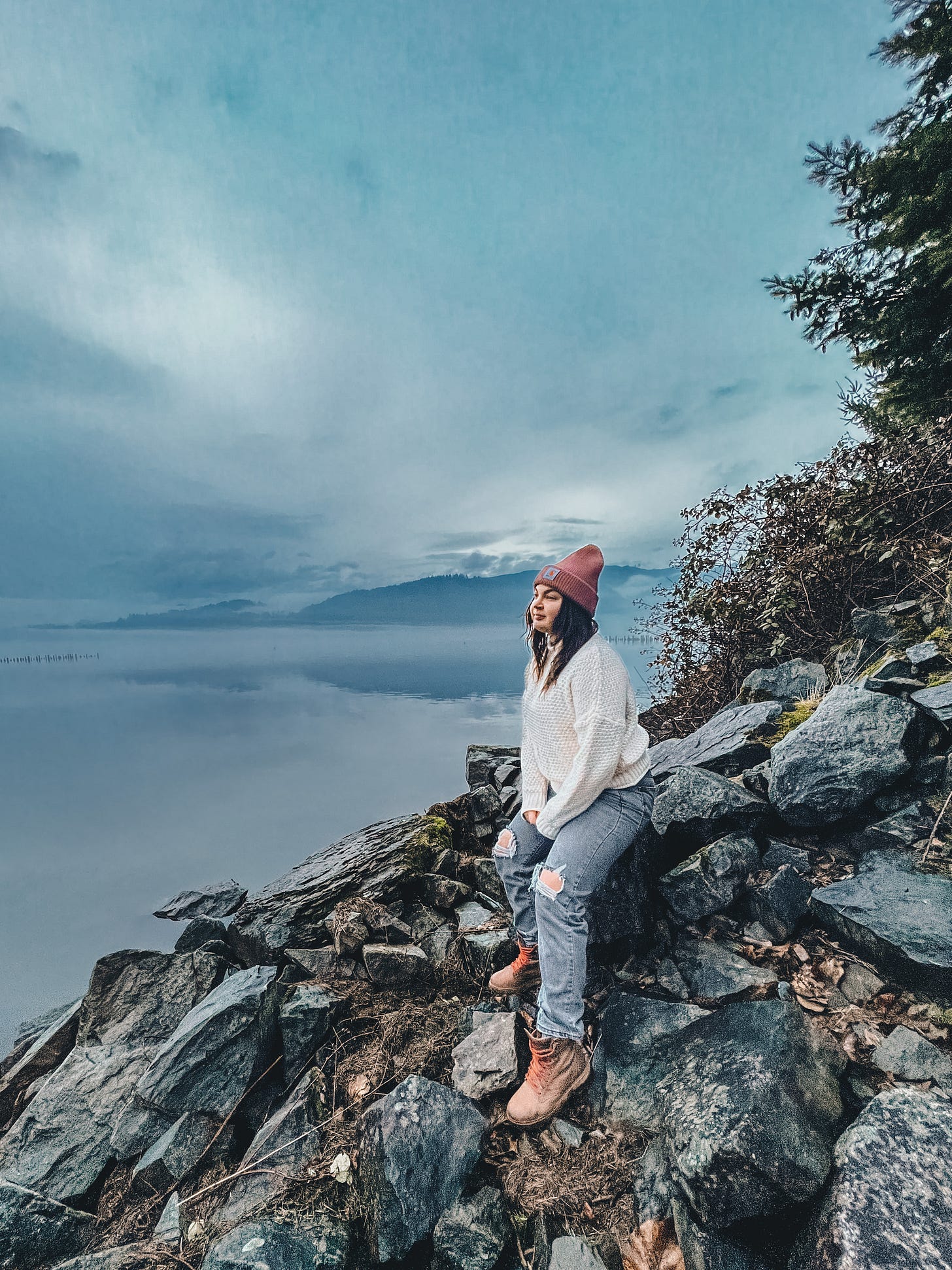 Author, Caitie, sitting on rocky shore gazing out over the water in reflection Author, Caitie, sitting on rocky shore gazing out over the water in reflection