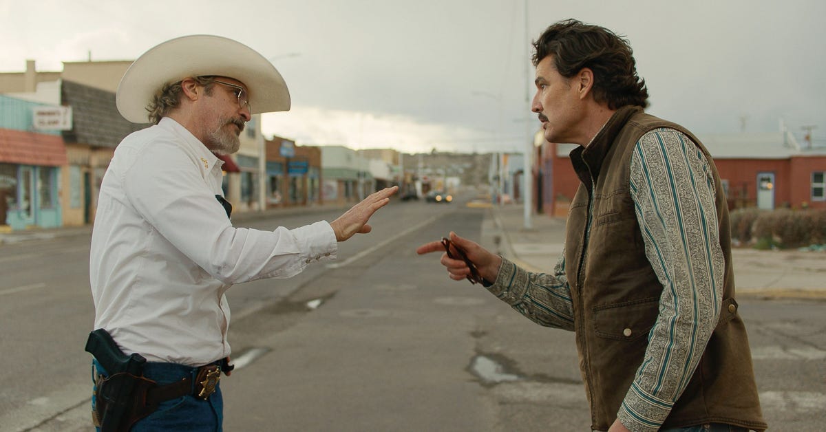 Joaquin Phoenix and Pedro Pascal arguing with each other in the middle of a small-town street, surrounded by buildings.