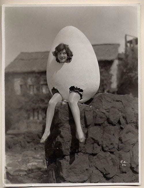 This may contain: a woman sitting on top of a rock next to an egg