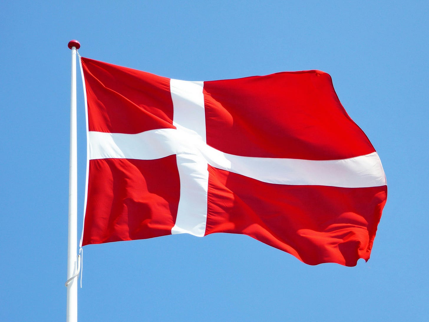 A photo of a Danish flag against a clear sky. A photo of a Danish flag against a clear sky.