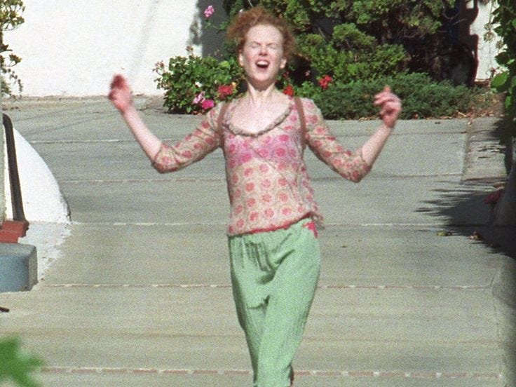 This may contain: a woman is walking down the sidewalk with her hands in the air while wearing green pants and a pink top