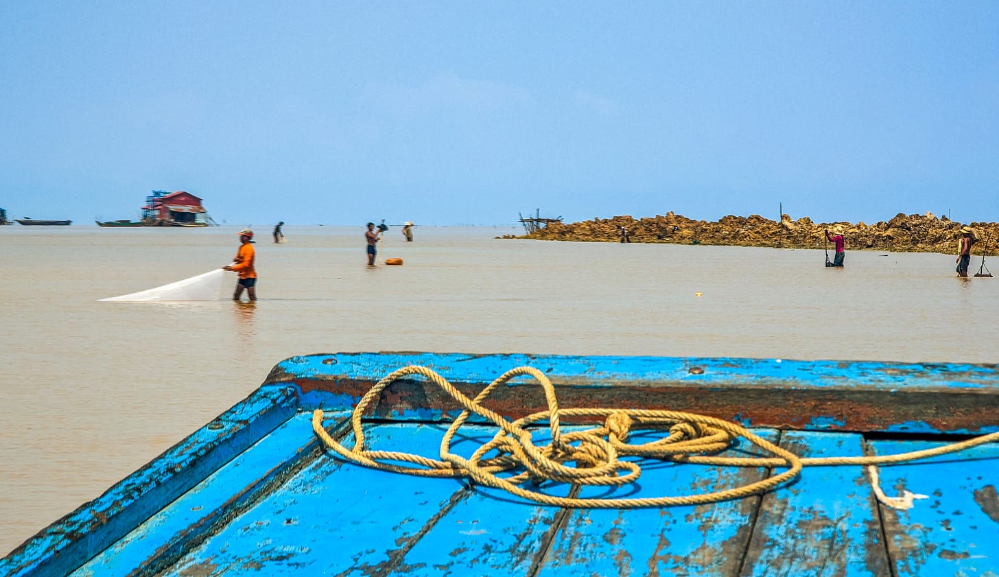 A photo of men standing in the shallows of the lake casting their nets into the water. 