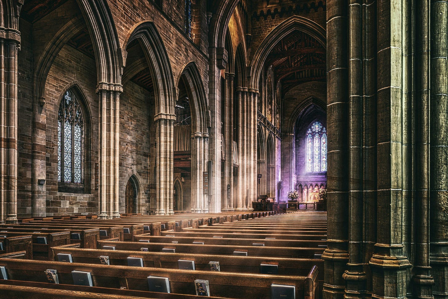 Image of the interior of a cathedral with sunbeams through the stain glass.