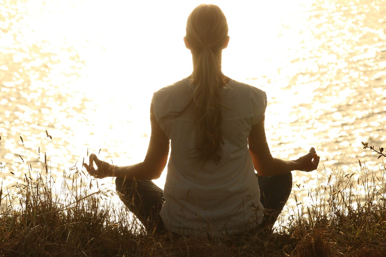 A view of the back of a woman sitting in the lotus position