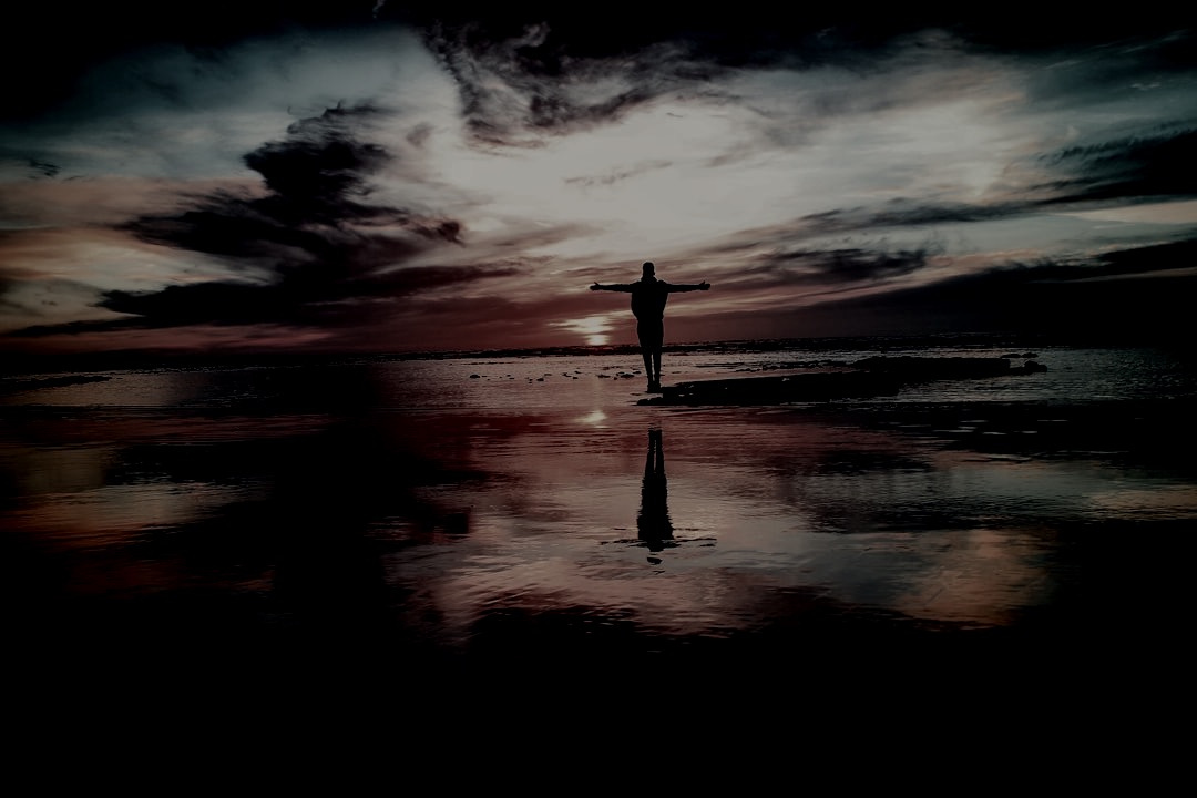 silhouette of person standing on rock surrounded by body of water