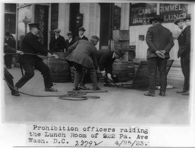 Prohibition agents raid a lunch room, standing among confiscated barrels and bottles of alcohol. Prohibition agents raid a lunch room, standing among confiscated barrels and bottles of alcohol.