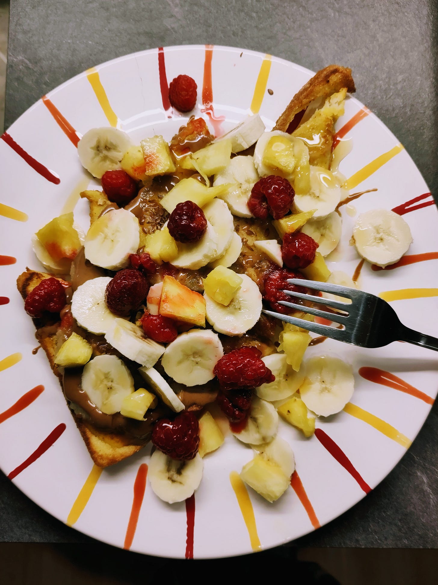 A plate of food showing homemade French toast with bananas, raspberries, pineapple, and almond butter.