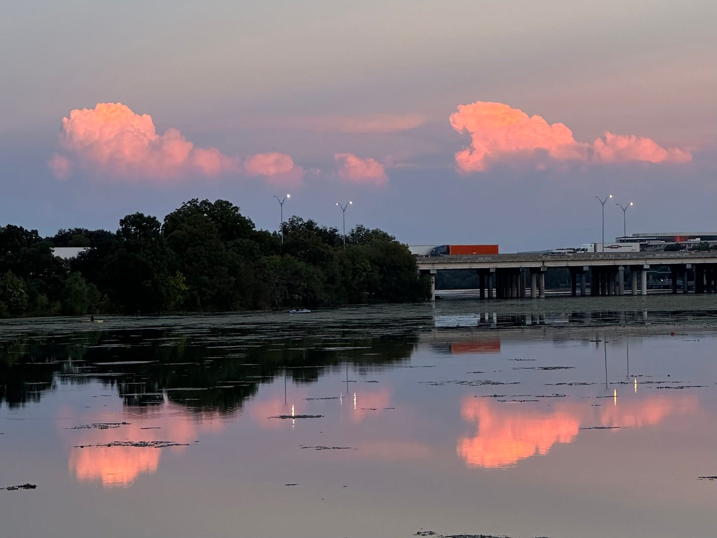 Pink clouds rise over the lake at sunset, reflected in the water below