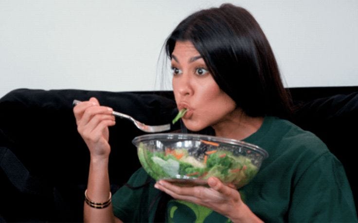 This may contain: a woman sitting on a couch eating salad from a bowl with a fork in her mouth