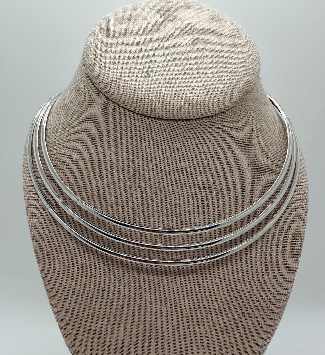 May include: A silver choker necklace with three layers of metal bands. May include: A silver choker necklace with three layers of metal bands.