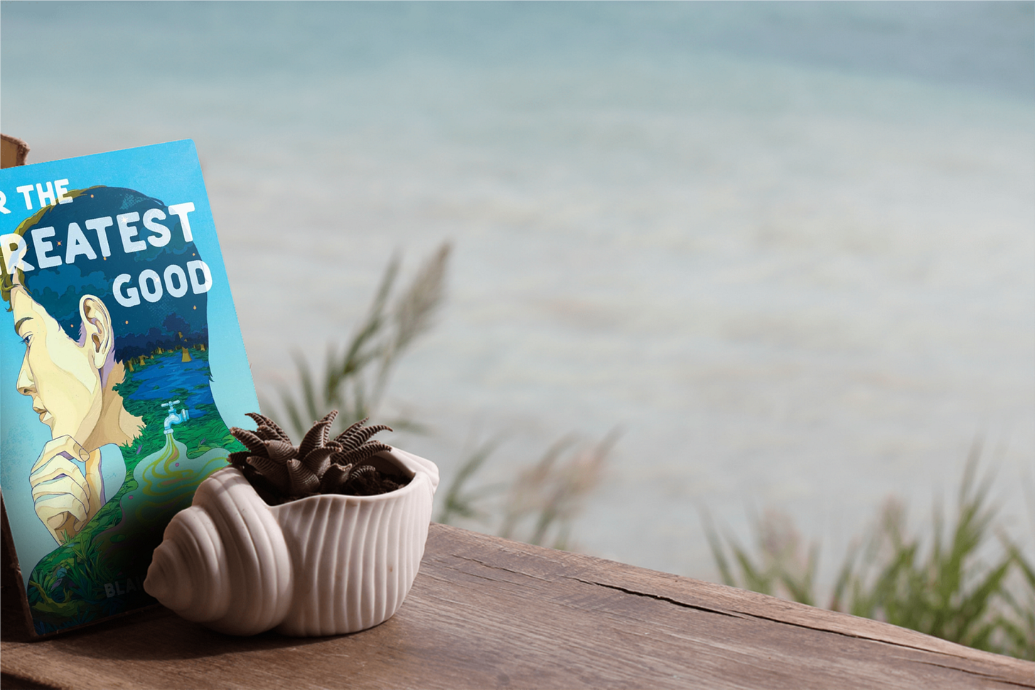 Book "For the Greatest Good" by Blair Hanson on a deck over looking a body of water