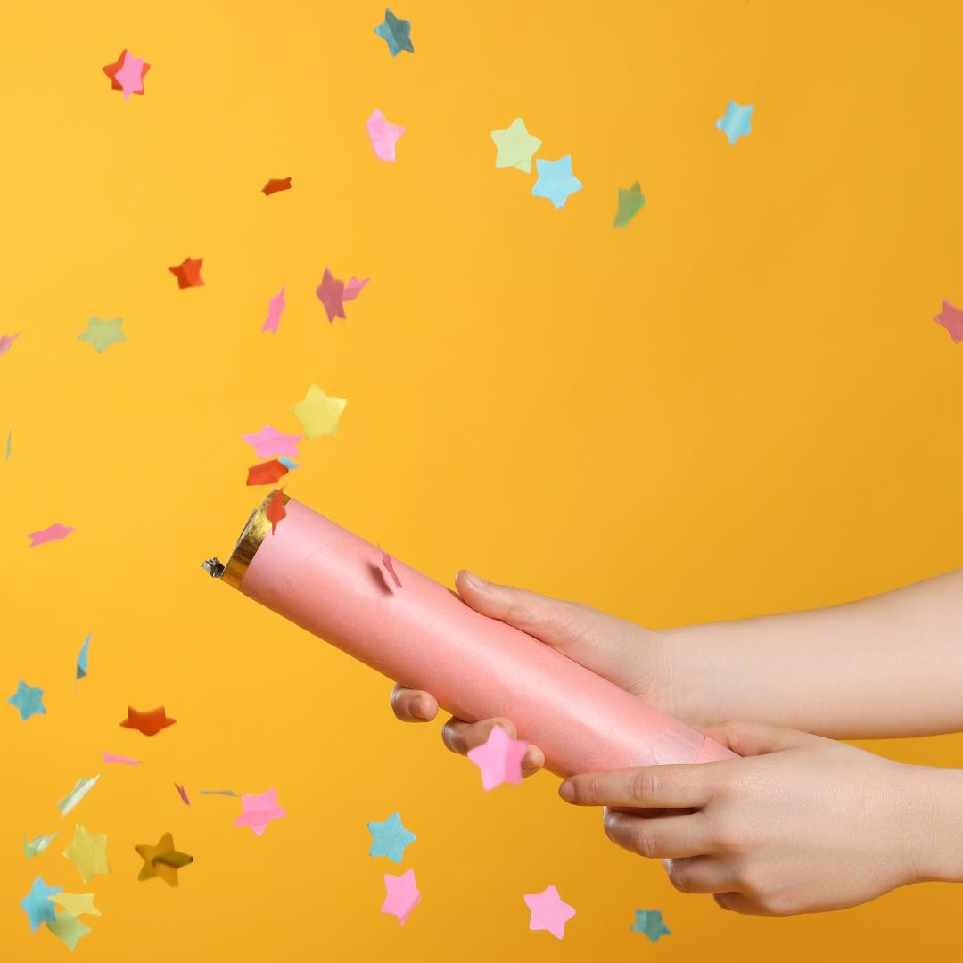 Hands holding what is creating an explosion of multi-coloured confetti in front of a yellow background.