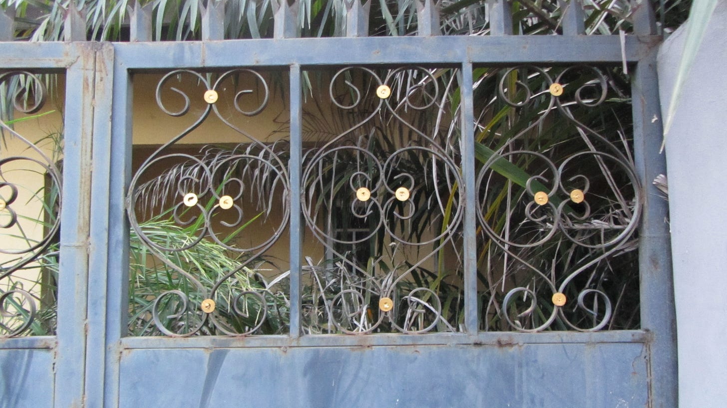 this is a dark blue gate with the sankofa heart symbol coiled out of iron near the top of it.