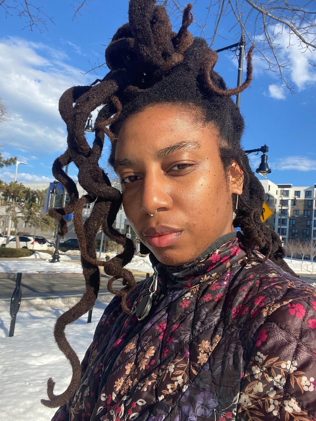 beautiful black woman with long curly freeform locs sits alone in a park on a bright winter day