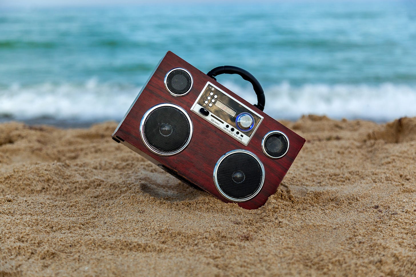 Vintage radio recorder on the sand at the beach. In the background waves wash the shore.