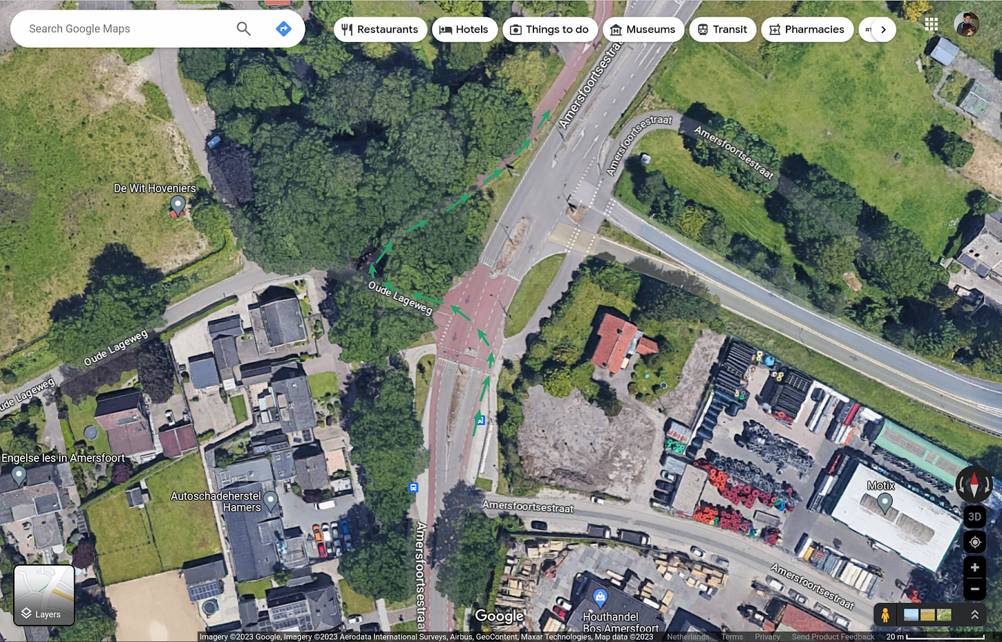 A google satellite view of a roadway depicting red on-street bike lanes transitioning to a red bike path on one side of the road. The transition intersection is coloured red.