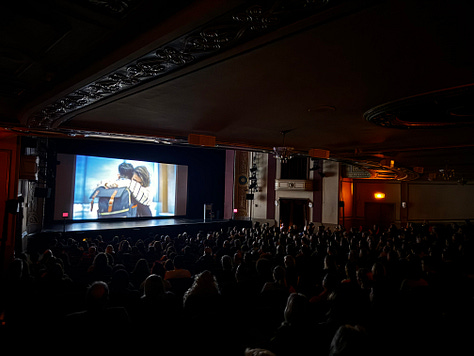 three photos of packed movie theaters screening "Come See Me in the Good Light." Giant screens with Andrea's face, or footage of Meg and Andrea hugging.