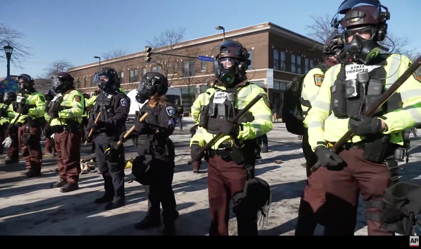 Community members are gathered wearing winter clothes and protective gear, chanting and holding signs, facing armed federal agents. Screenshot of AP Livestream from January 24, 2026 Community members are gathered wearing winter clothes and protective gear, chanting and holding signs, facing armed federal agents. Screenshot of AP Livestream from January 24, 2026