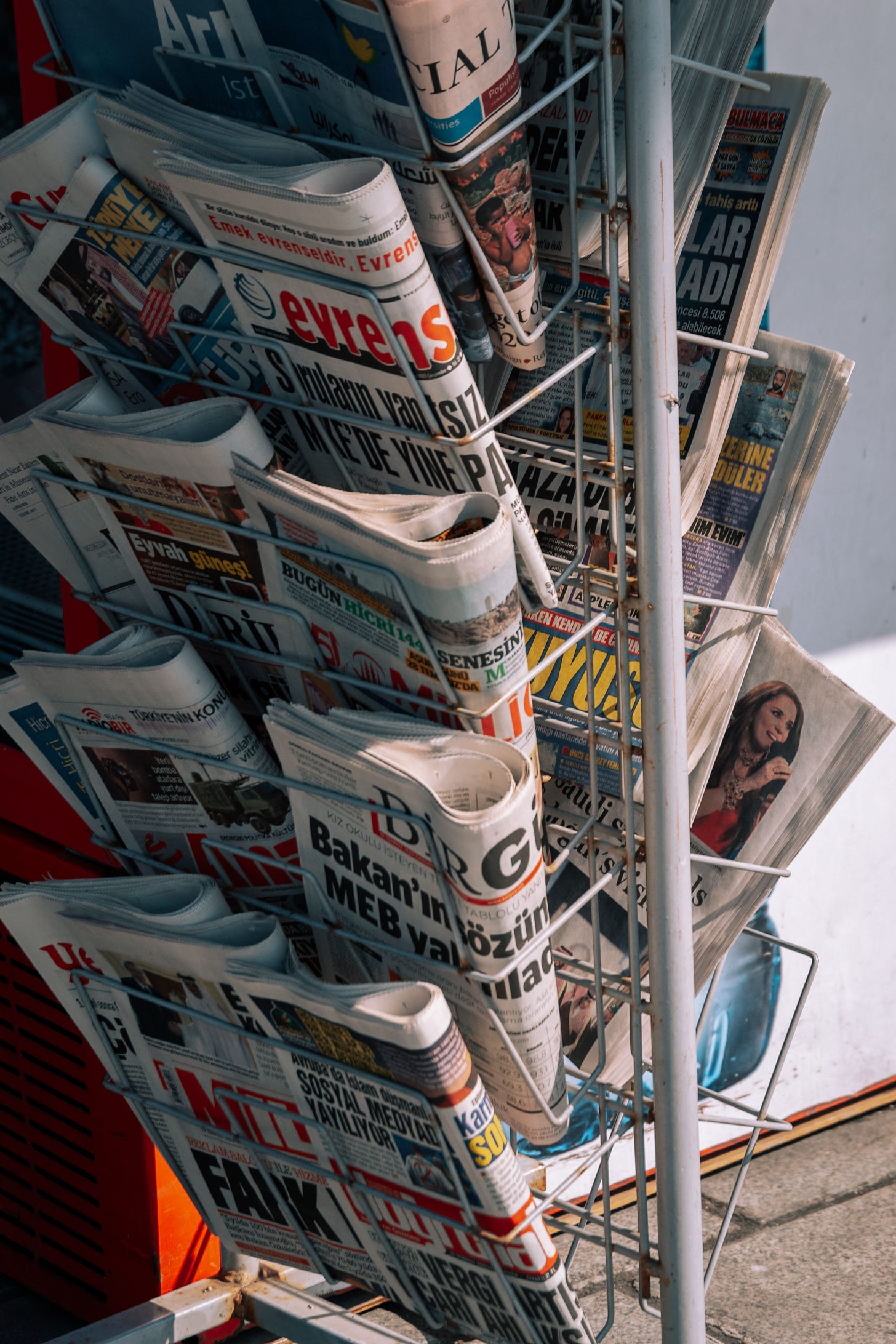 A close-up shot of a white wire display rack filled with various printed international newspapers and news daily editions on a street newsstand. A close-up shot of a white wire display rack filled with various printed international newspapers and news daily editions on a street newsstand.