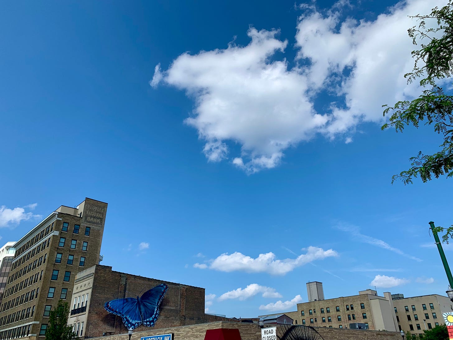 White clouds floating through a blue sky; one of the buildings in the skyline beneath has a blue butterfly painted on its side