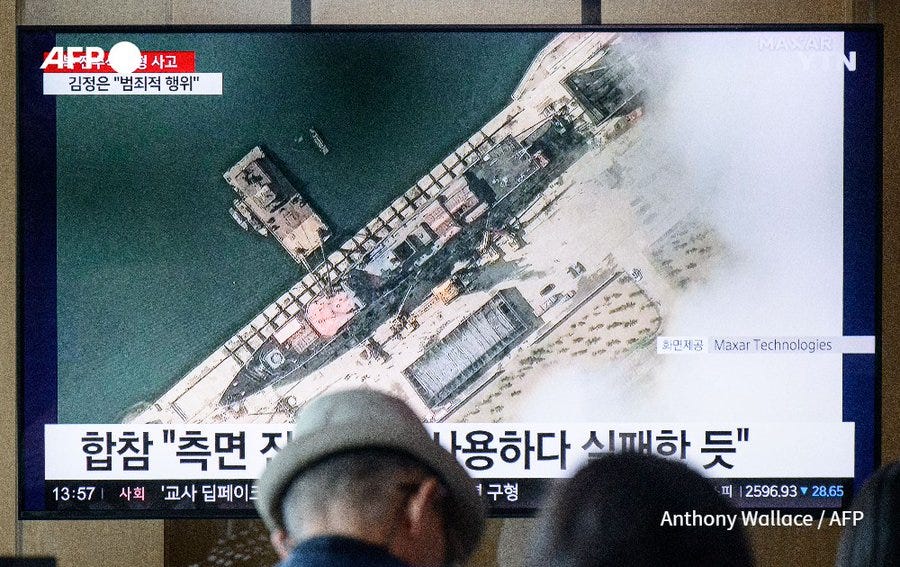 In a photo taken in Seoul on May 22, 2025, people sit near a television showing news footage with a satellite still image courtesy of Maxar Technologies showing a general view of a North Korean warship at a harbour ahead of its launch (Anthony Wallace / AFP)