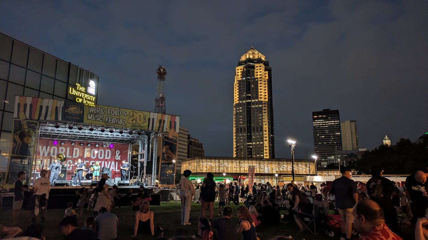 Western Gateway Park at dusk facing 801 Grand and during last years World Food and Music Festival. The photo features the music stage and the audience.
