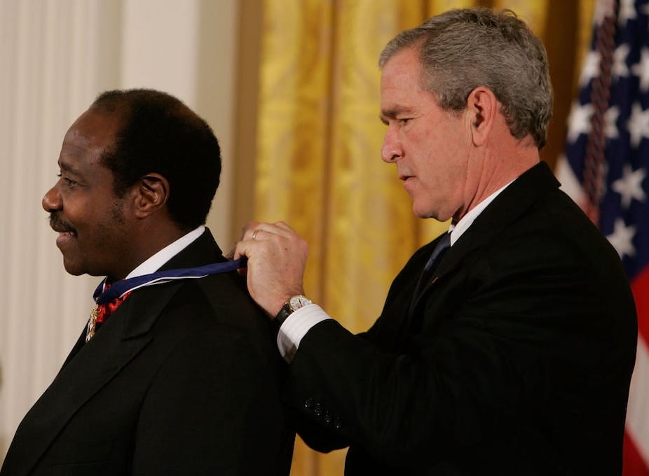 A man tying a ribbon around another man's neck, with the American flag behind them A man tying a ribbon around another man's neck, with the American flag behind them