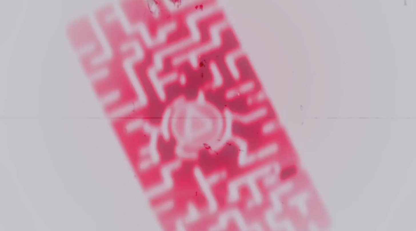 A rectangular device that looks like a computer chip that has a round emblem in the center with a triangle on it. It is tinted red.