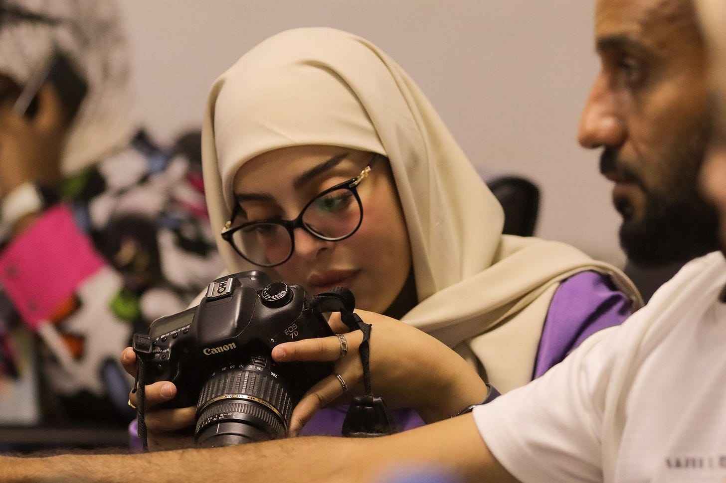 A woman wearing hijab looks into the view screen of the camera she is holding. A woman wearing hijab looks into the view screen of the camera she is holding.