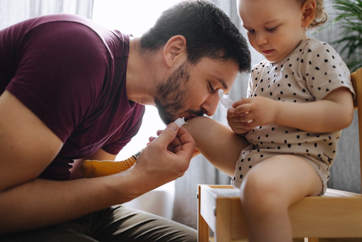 Father kissing his young child's knee after an injury. Father kissing his young child's knee after an injury.