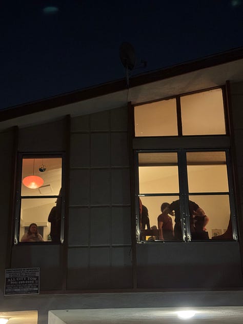 Photo 1: People gathering in a living room with vaulted ceilings. Photo 2: A painting and 3 drawings hung on a wall. Photo 3: A surrealist painting of amorphous creatures hanging from a tree. Photo 4: People gathered around the surrealist painting. Photo 5: A collage with cartoon images of a trail to the ocean and a butterfly, and bold text reading: traces of a path, losing sight of the sea. Photo 6: People and a red dog gathered around a man playing guitar. Photo 7: Ink and pastel drawings of two circles meeting. Photo 8: a pile of shoes at a door. Photo 9: Silhouettes of people through tall windows from outside at night.