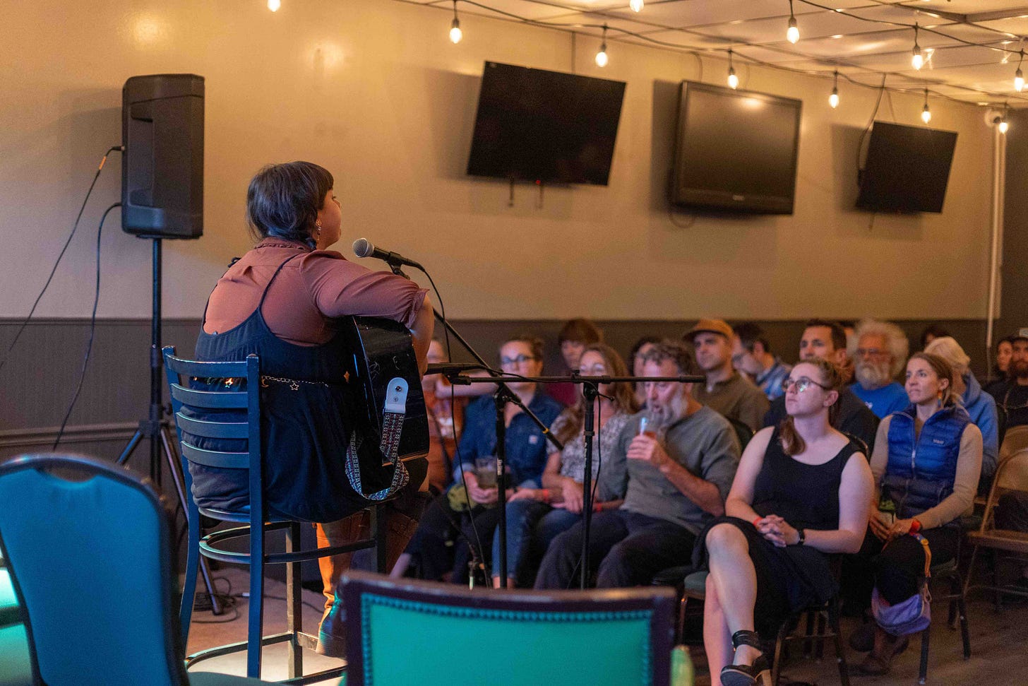 woman on stage with guitar seen from behind as audience watches