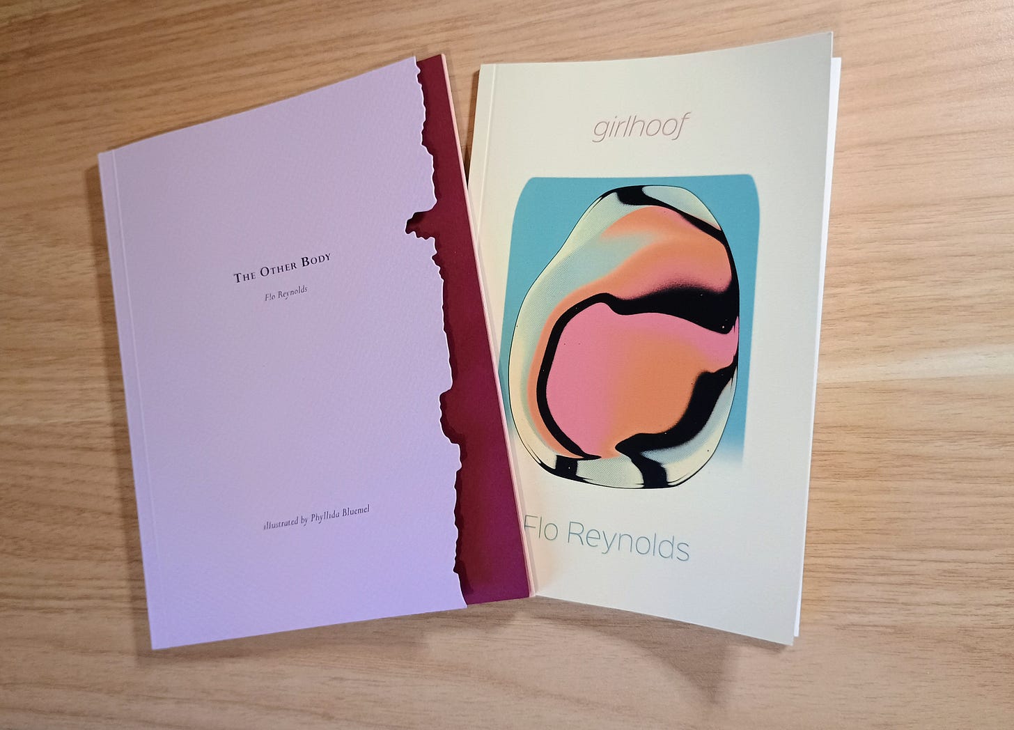 A flat lay of The Other Body and girlhoof by Flo Reynolds on a wooden table.