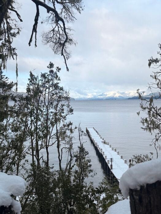 Snow-covered dock extending into calm lake with snowy mountains in background Snow-covered dock extending into calm lake with snowy mountains in background