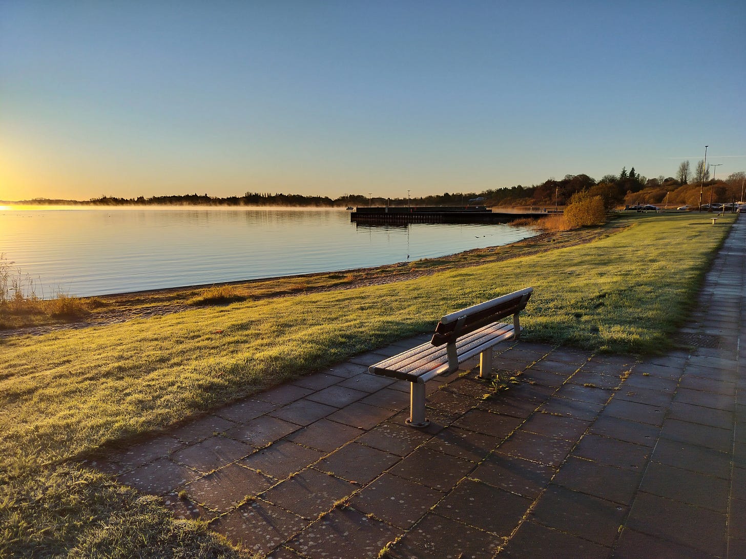 Frost-covered bench facing a still misty lake at dawn in Ireland Frost-covered bench facing a still misty lake at dawn in Ireland