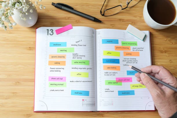 Hand of a woman writing appointments in a diary organizer or schedule calendar with a lot of colorful sticky notes for her time management on a wooden desk with coffee, flowers and glasses, selected focus Hand of a woman writing appointments in a diary organizer or schedule calendar with a lot of colorful sticky notes for her time management on a wooden desk with coffee, flowers and glasses, selected focus, narrow depth of field managing your life stock pictures, royalty-free photos & images