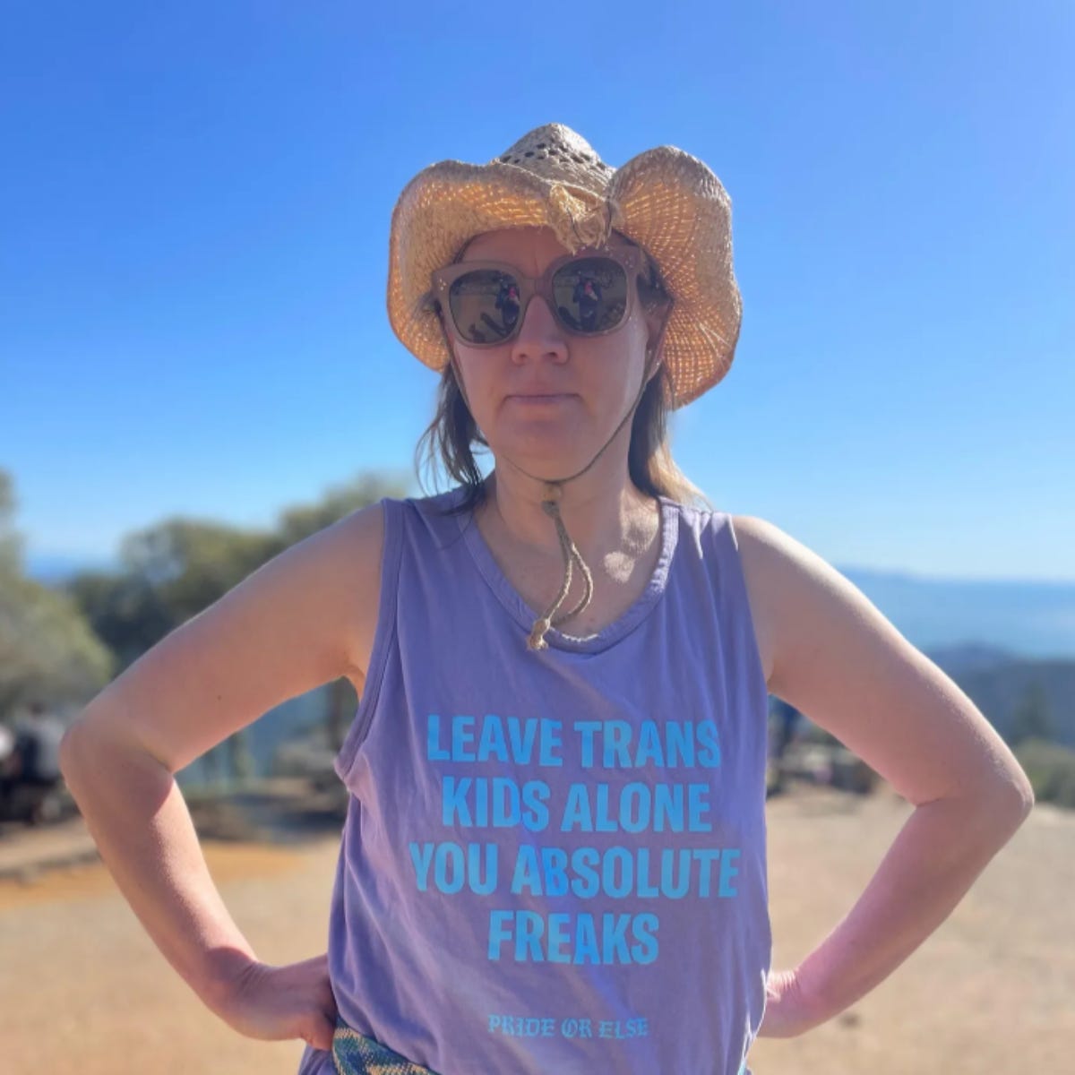 Cowgirl in sunglasses wears a tank top that says "Leave Trans Kids Alone, You Absolute Freaks." Cowgirl in sunglasses wears a tank top that says "Leave Trans Kids Alone, You Absolute Freaks."