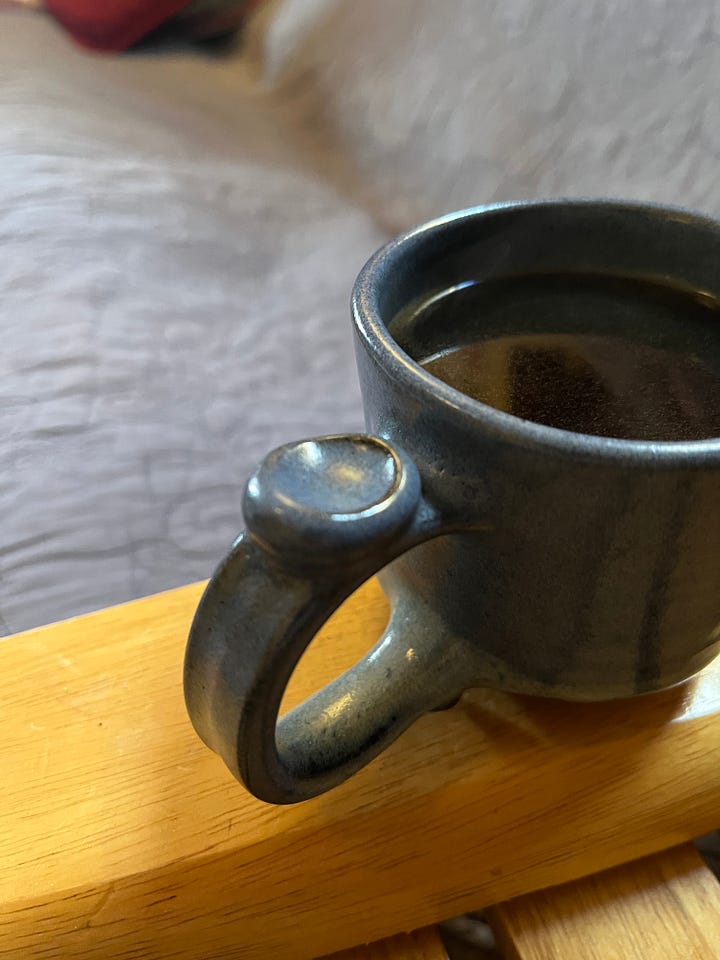 two pottery mugs, one blue and squat, one gray and skinny. Both have a dot of clay at the top of the handle upon which to rest your thumb