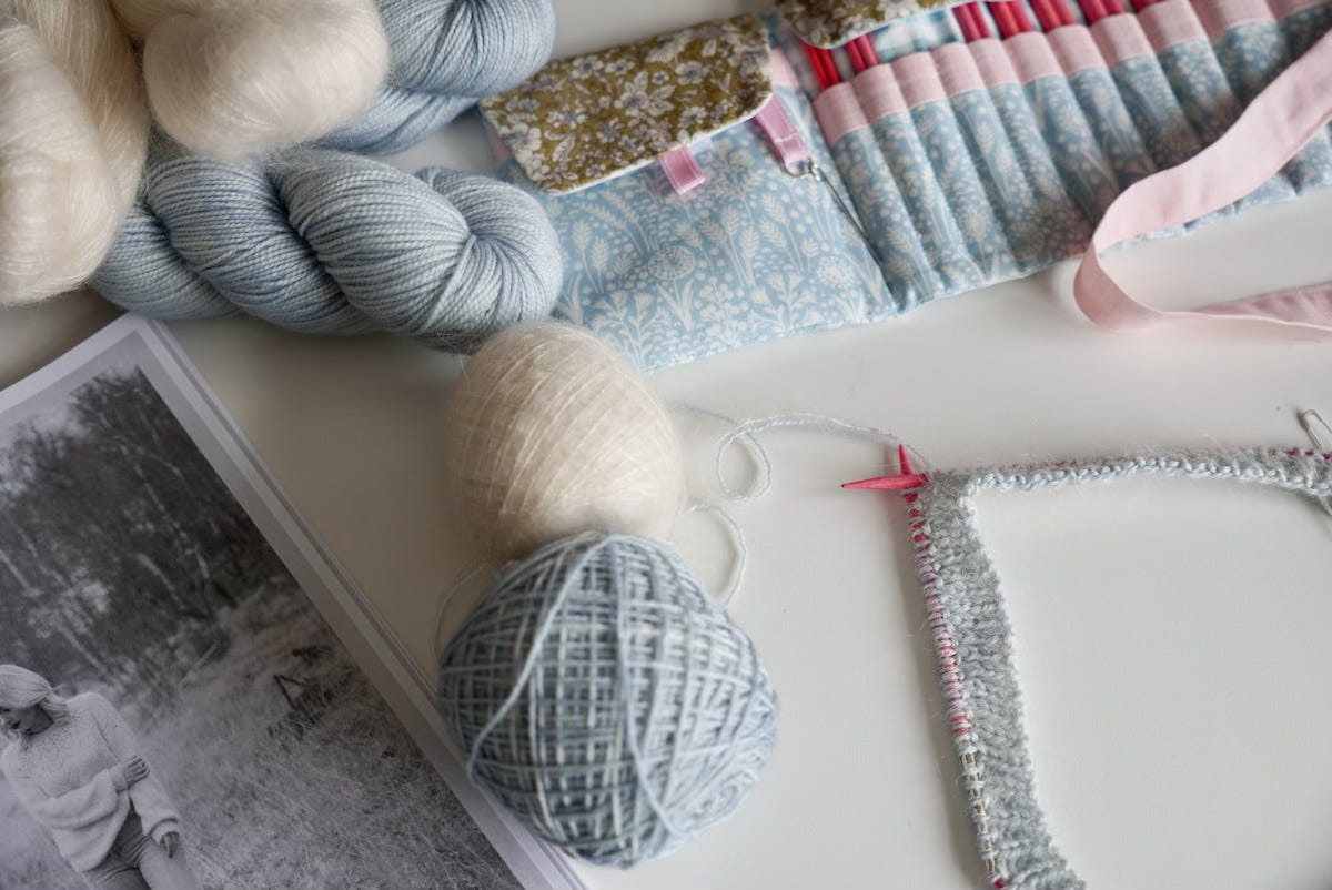 Circular knitting needles with an inch of ribbing worked.  Surrounded by the Whitmoor Sweater pattern, yarn and a set of interchangeable knitting needles.