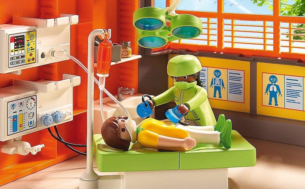 A colorful Playmobil hospital playset with a patient doll lying on an operating table as a doctor doll prepares to zap it with a defibrillator