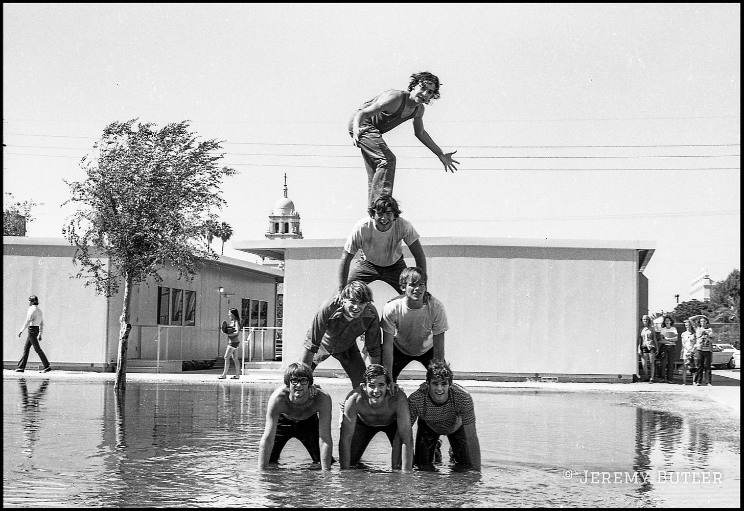 Seven young men forming a human pyramid standing in irrigation water in black and white.