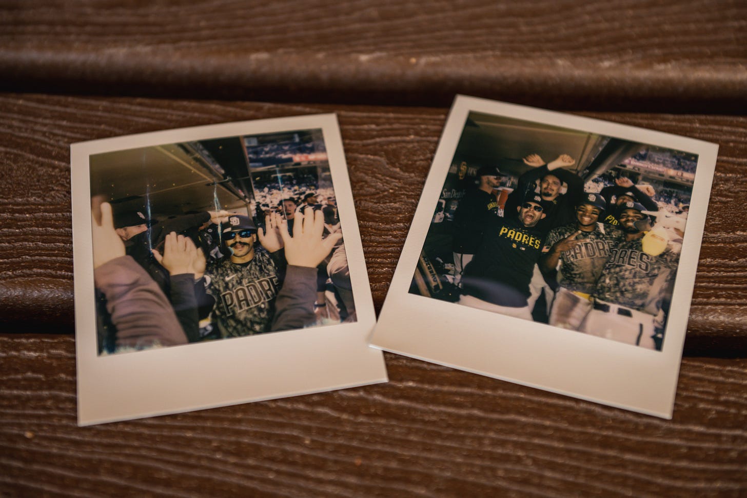 Two polaroid photos on the bench in the Padres dugout. The Polaroid on the left is a photo of Trent Grisham smiling as he high fives teammates following his home run. The Polaroid on the right is a photo of Xander Bogaerts, José Azocar, Nick Martinez, Blake Snell and Josh Hader. Xander and José are smiling and holding up peace signs for the camera. Nick is smiling and yelling in celebration with his arms wide. Blake and Josh hold their arms in an "X" above their heads. 