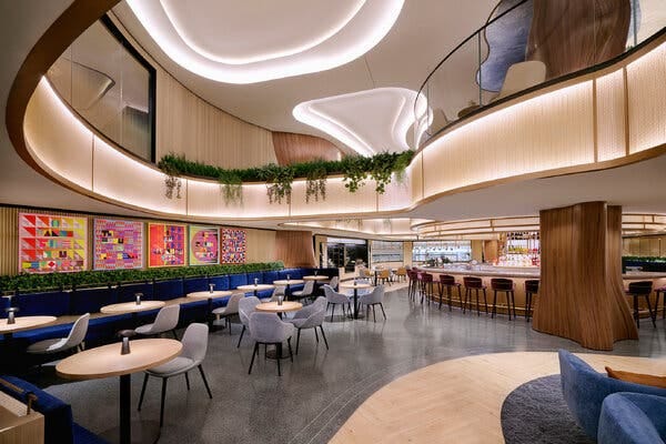 The interior of a two-story airport lounge with chairs and tables, colorful wall art and brightly lit bar. The interior of a two-story airport lounge with chairs and tables, colorful wall art and brightly lit bar.